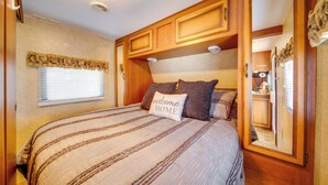 Un dormitorio con cama, ventana con persianas, armarios de madera y un espejo.