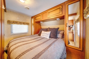 Ein Schlafzimmer mit einem Bett, einem Fenster mit Jalousien, Holzschränken und einem Spiegel.
