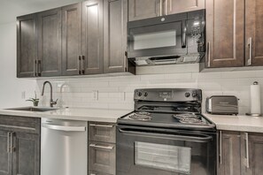 A kitchen with dark wooden cabinets, a stainless steel microwave, a gas stove, and a toaster. - FIU Basecamp: Miami Home w/ Fenced Yard! (Miami)