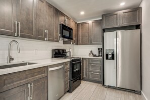 A modern kitchen with stainless steel appliances, wooden cabinets, and a white countertop. - FIU Basecamp: Miami Home w/ Fenced Yard! (Miami)