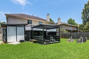 Een achtertuin met een terras, tuinmeubilair en een huis op de achtergrond.