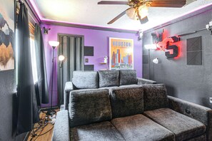 A room with a grey sofa, a ceiling fan, and a poster of Houston, Texas. - Games & Yard! Family Home Near Kemah Boardwalk (Dickinson)