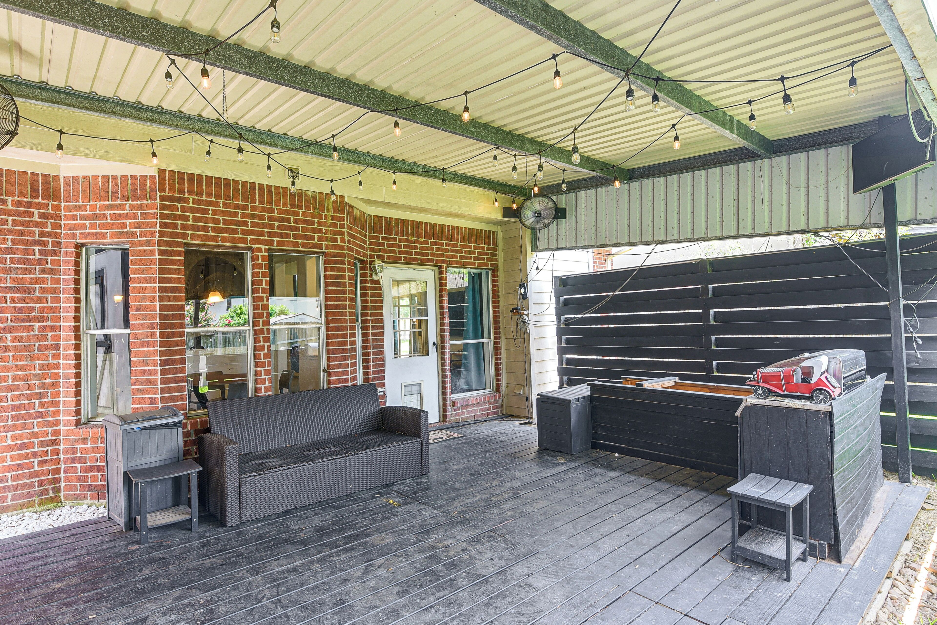 A covered outdoor area with a brick building, a wicker sofa, a barbecue grill, and string lights.