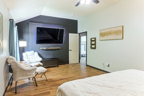 Een slaapkamer met een bed, een stoel, een televisie en een deur naar een andere kamer.