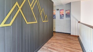A hallway with a wooden floor, a grey wall with yellow geometric patterns, and a staircase with white balusters. - Games & Yard! Family Home Near Kemah Boardwalk (Dickinson)