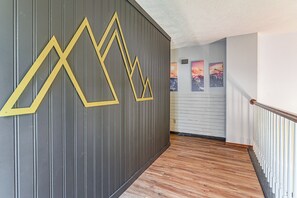 A hallway with a wooden floor, a grey wall with yellow geometric patterns, and a staircase with white balusters. - Games & Yard! Family Home Near Kemah Boardwalk (Dickinson)