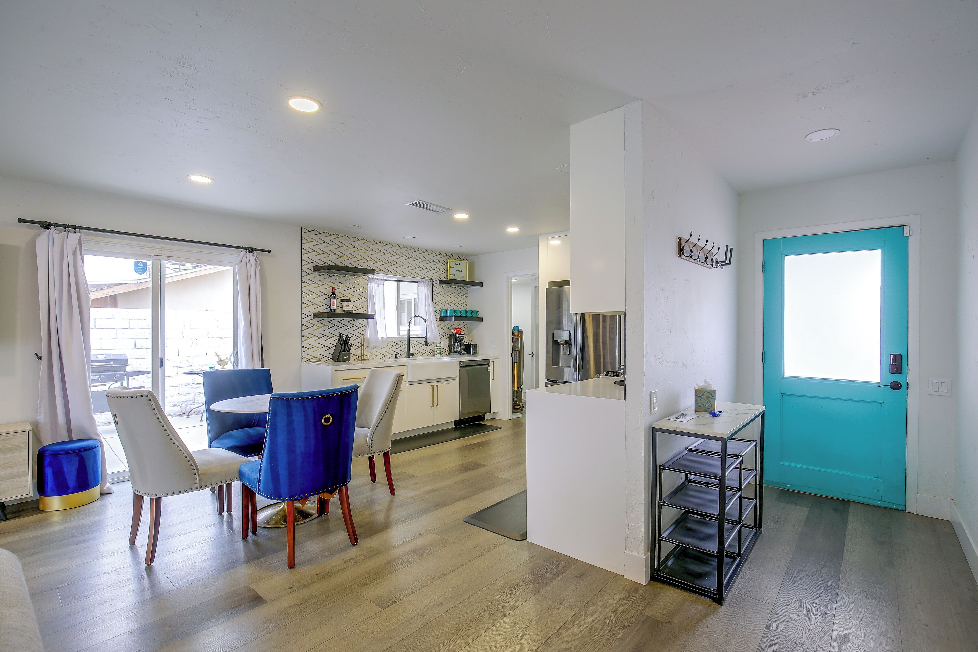 A modern kitchen with white cabinets, a blue door, and a dining area with blue chairs.
