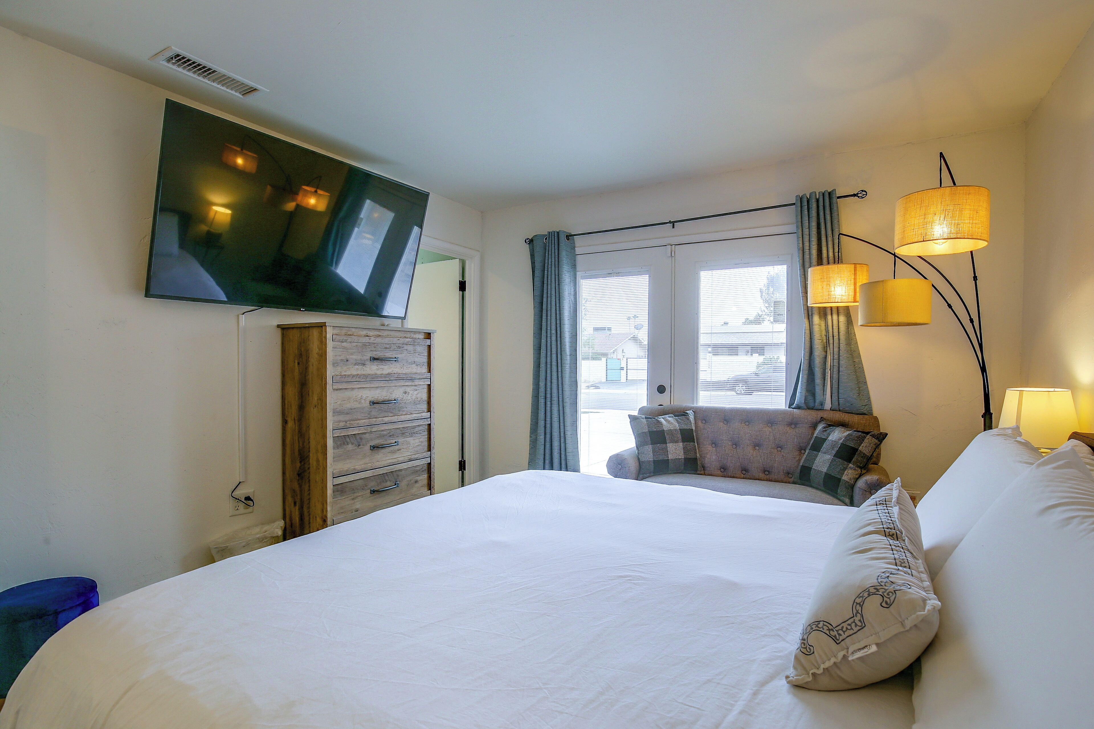 Een hotelkamer met een bed, een aan de muur bevestigde televisie, een dressoir en een raam met gordijnen.