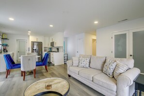 A modern living room with a beige sofa, blue chairs, a coffee table, and a kitchen area with a refrigerator and microwave. - Grill & Fire Pit! Palm Desert Extended Escape (Palm Desert)