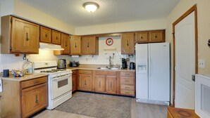 A compact kitchen with wooden cabinets, a stove, a refrigerator, and a coffee maker.