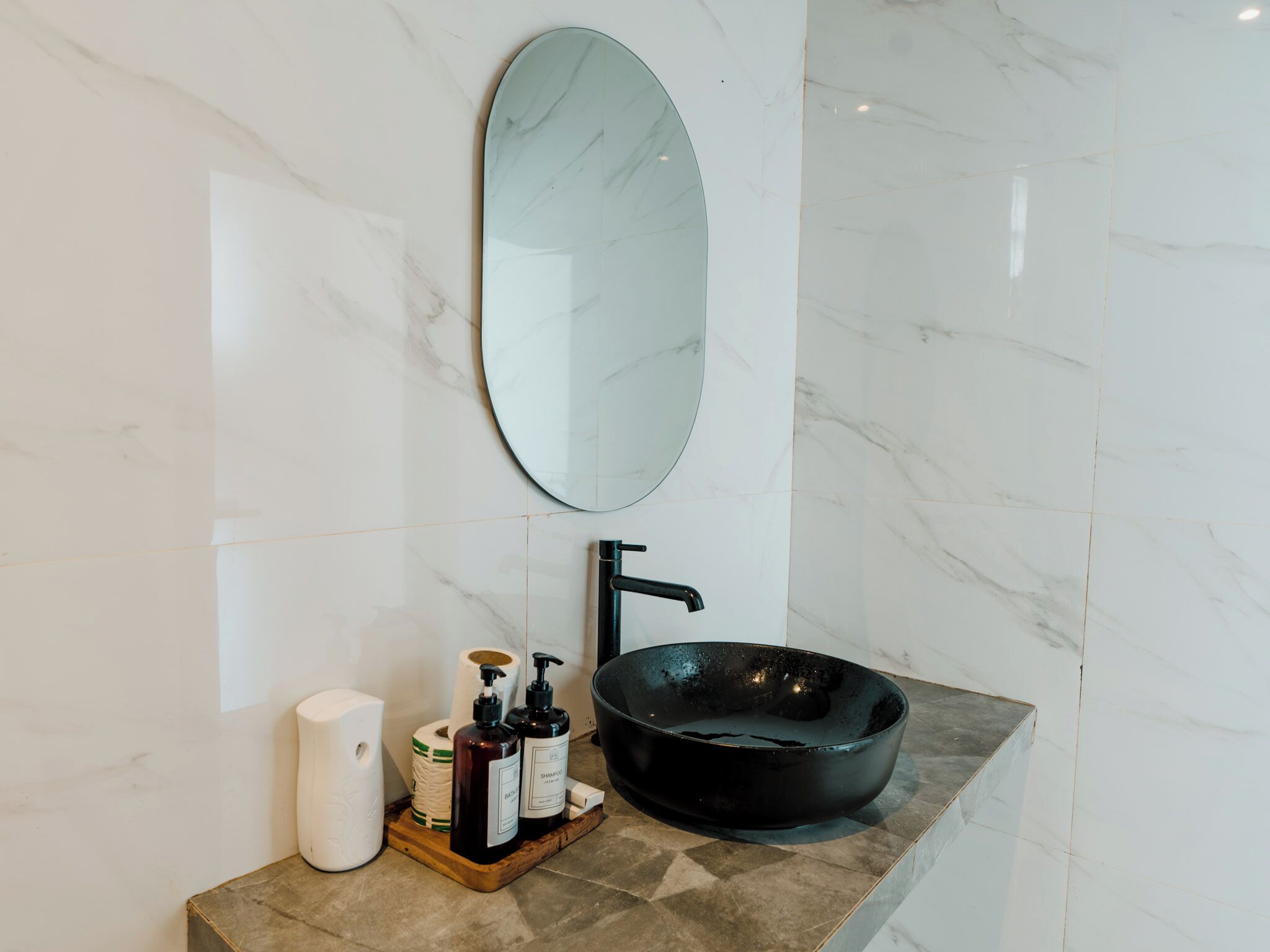 Baño con pared de mármol, lavabo negro y espejo.