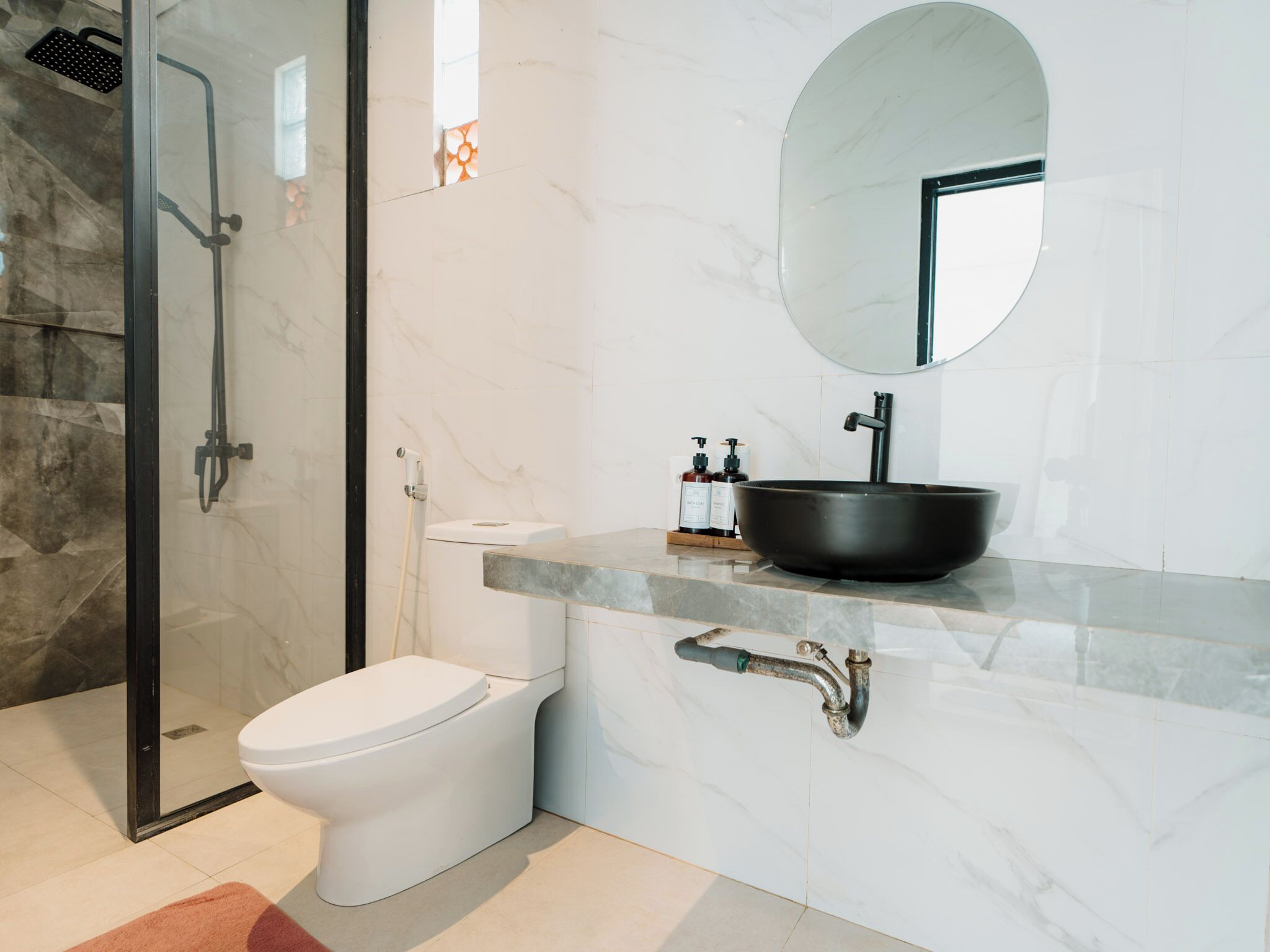 A modern bathroom with a toilet, a black sink, a mirror, and a shower area.