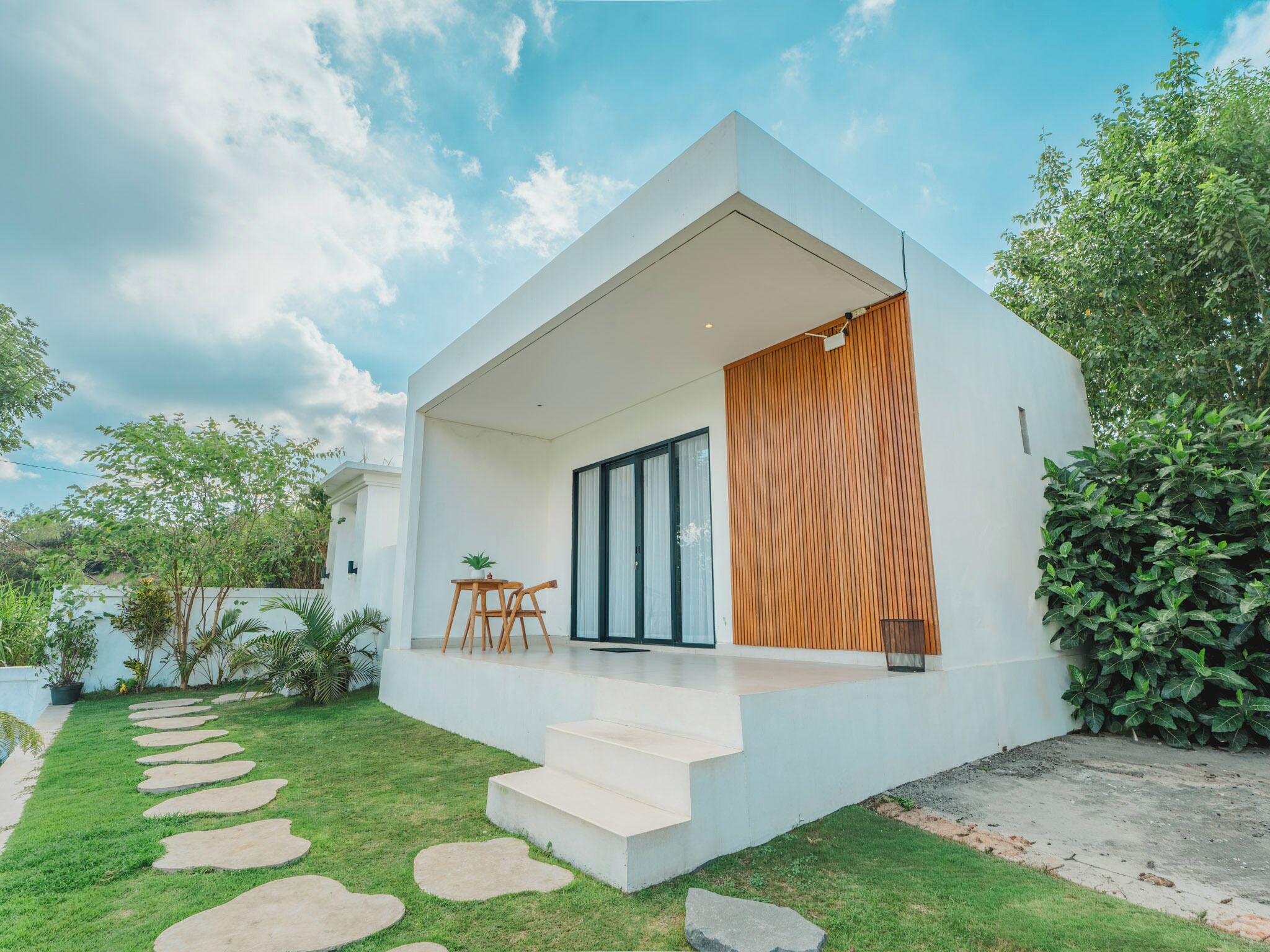 Una casa moderna con techo plano, pared de listones de madera y un pequeño espacio exterior con mesa y sillas.