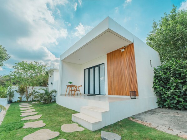 A modern house with a flat roof, a wooden slatted wall, and a small outdoor seating area with a table and chairs.