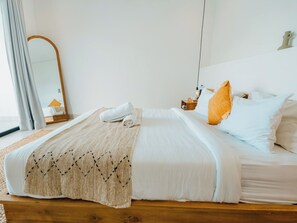 A neatly made bed with white linens, a beige throw blanket, and a wooden headboard.