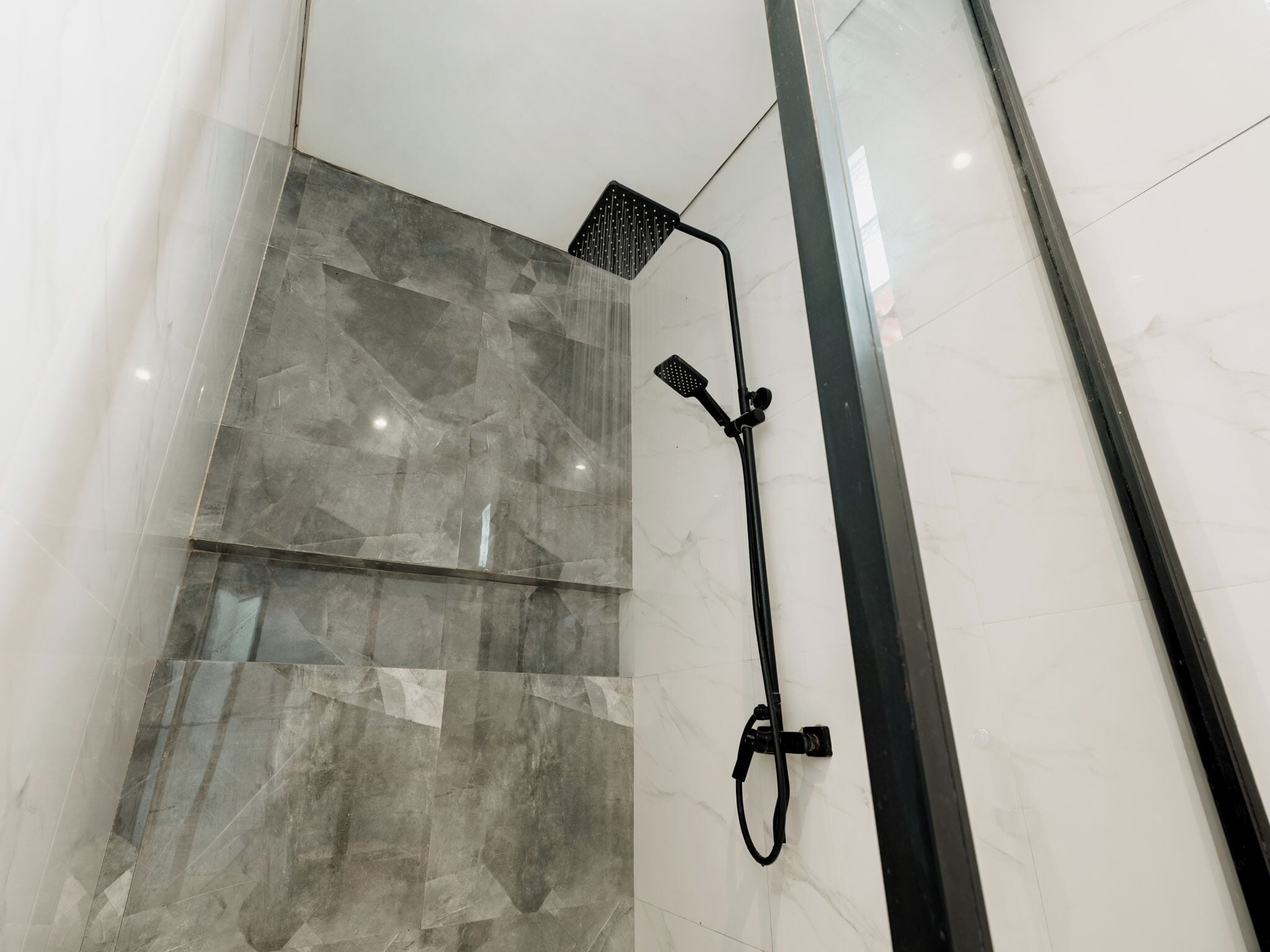 A modern shower with a handheld showerhead and a wall-mounted rain showerhead.