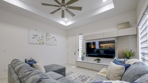 Ein modernes Wohnzimmer mit einem Flachbildfernseher, grauen Sofas und Kunstwerken an den Wänden.