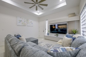Ein modernes Wohnzimmer mit einem Flachbildfernseher, grauen Sofas und Kunstwerken an den Wänden.