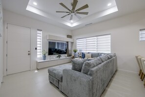 A modern living room with a grey sectional sofa, a flat-screen TV, and a ceiling fan. - Modern McAllen Townhome: 4 Mi to Dtwn (McAllen)
