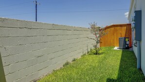 Ein Wohnhausgarten mit einer Betonmauer, einem Holzzaun, einem kleinen Baum und einer Klimaanlage.