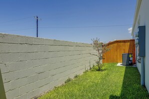 Ein Wohnhausgarten mit einer Betonmauer, einem Holzzaun, einem kleinen Baum und einer Klimaanlage.