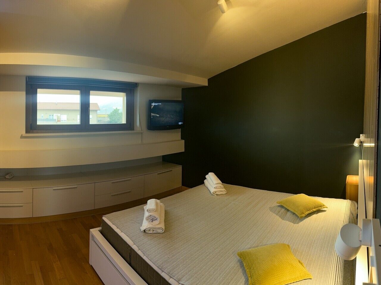 Um quarto com cama, janela, televisão e mesa de cabeceira.