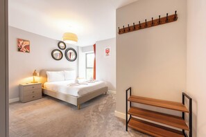Ein Schlafzimmer mit einem Bett, einem Nachttisch, einer Lampe, einem wandmontierten Spiegel und einem Kleiderständer.