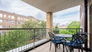 En balkon med et bord og stole, en murstenssøjle og udsigt til boligbygninger.