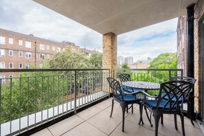Ein Balkon mit Tisch und Stühlen, einer Ziegelstütze und Blick auf Wohnhäuser.