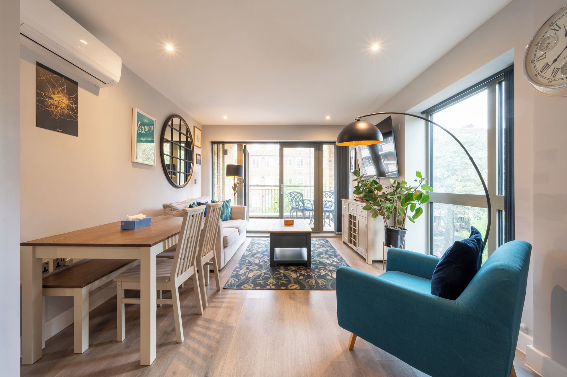 Ein modernes Wohnzimmer mit einer Couch, einem Essbereich mit Tisch und Stühlen, einem großen Fenster mit Blick und einer Uhr an der Wand.