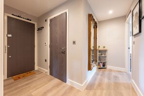 Ein Flur mit Holzboden, einer Tür mit Schlüsselloch, einem an der Wand befestigten Lichtschalter und einem Regal mit Büchern und Dekoration.