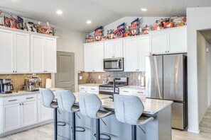 A modern kitchen with white cabinets, a stainless steel refrigerator, a microwave, and a bar area with stools. - 3 Mi to Spokane River! Furnished Patio & Yard (Post Falls)