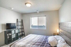 A bedroom with a bed, a television on a stand, a window with blinds, and a nightstand with a lamp. - 3 Mi to Spokane River! Furnished Patio & Yard (Post Falls)