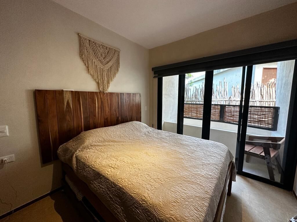 Une chambre à coucher avec une tête de lit en bois, un grand lit recouvert d’une courtepointe à motifs, et une porte-fenêtre coulissante donnant sur un espace extérieur.