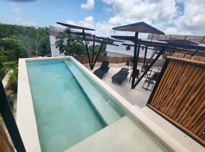 A rectangular swimming pool with lounge chairs and a wooden fence. - Condominium in Tulum, Mexico (Tulum)