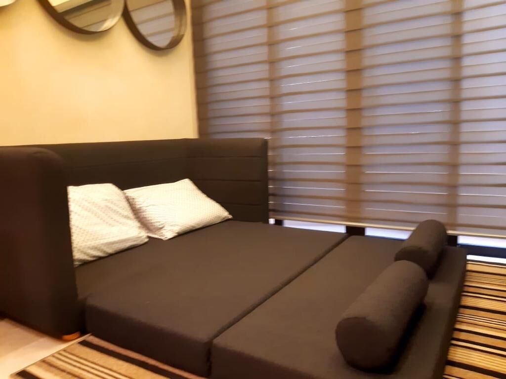 A bed with a headboard, a bedside table, and a window with blinds.