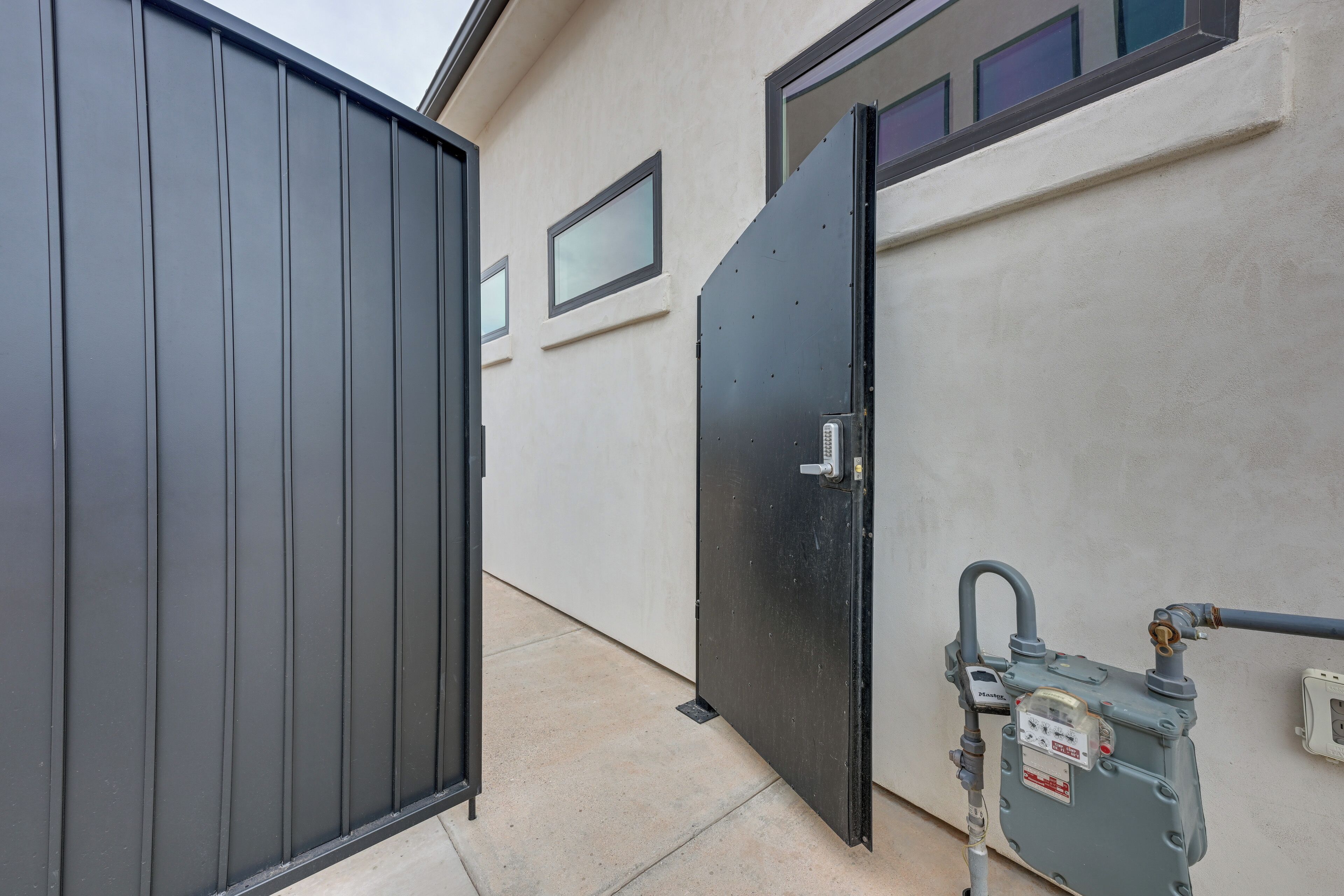 A gated entrance with a metal gate and a door, a concrete pathway, and a utility meter on the right. - Resort-Style St George Casita w/ Lagoon Access (St. George)