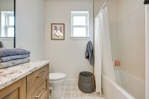 Ein Badezimmer mit Marmorplatte, Toilette, einem Korbwäschesammler und einer Duschvorhang.