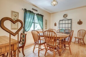 A dining room with a wooden table and chairs, a heart-shaped wooden object, and a window with curtains. - Walk to Canyon Lake! Family Haven w/ Yard & Patio (Canyon Lake)