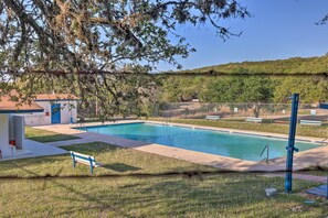 Ein Schwimmbecken mit blauer und weißer Liegefläche, umgeben von einem Zaun und Bäumen.