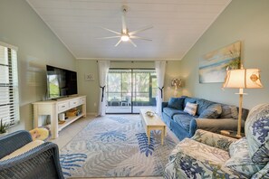 A living room with a television, sofas, a ceiling fan, and a view through a glass door. - Walk to the Gulf Coast! 55+ Retreat w/ Pool Access (Englewood)