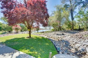 A landscaped garden with a variety of trees, a clear sky, and a body of water in the background. - Hot Tub, Game Room, Playset & Fire Pits! (Redding)