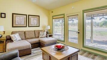A living room with a sectional sofa, a coffee table, a ceiling fan, and a large sliding glass door leading to an outdoor area.