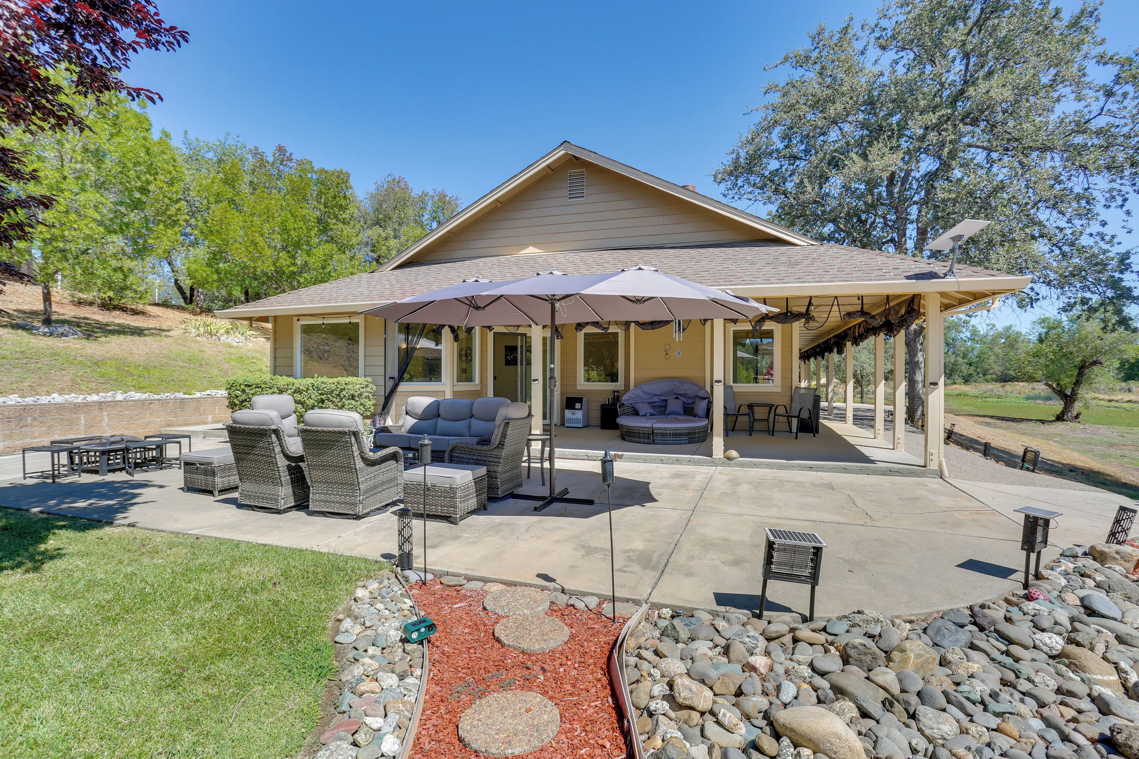 Un patio techado con mobiliario exterior, una pérgola y un jardín ajardinado con rocas y acolchado.