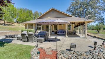 Un patio techado con mobiliario exterior, una pérgola y un jardín ajardinado con rocas y acolchado.