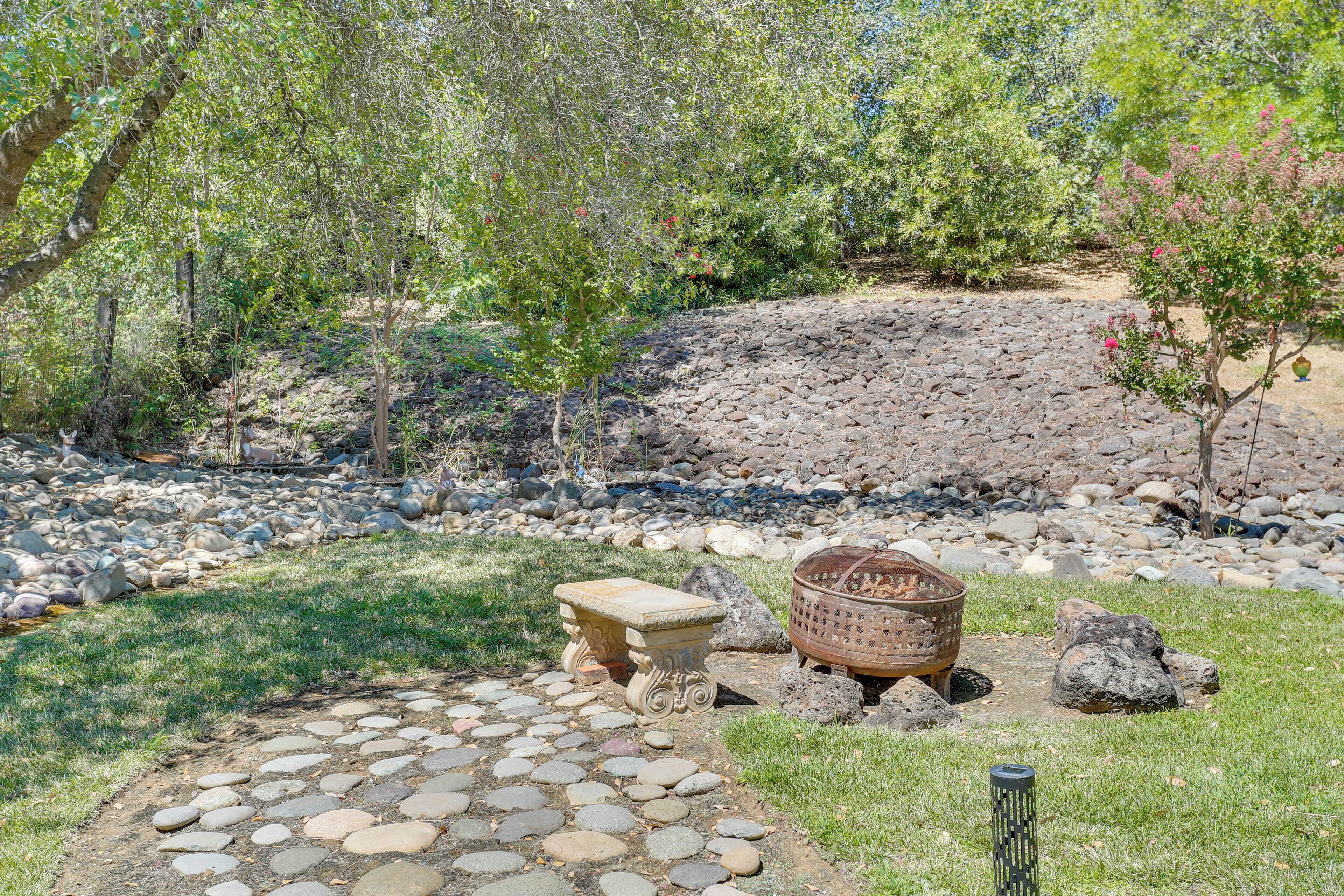 A garden with a stone pathway, a rustic fire pit, and a small stone table.