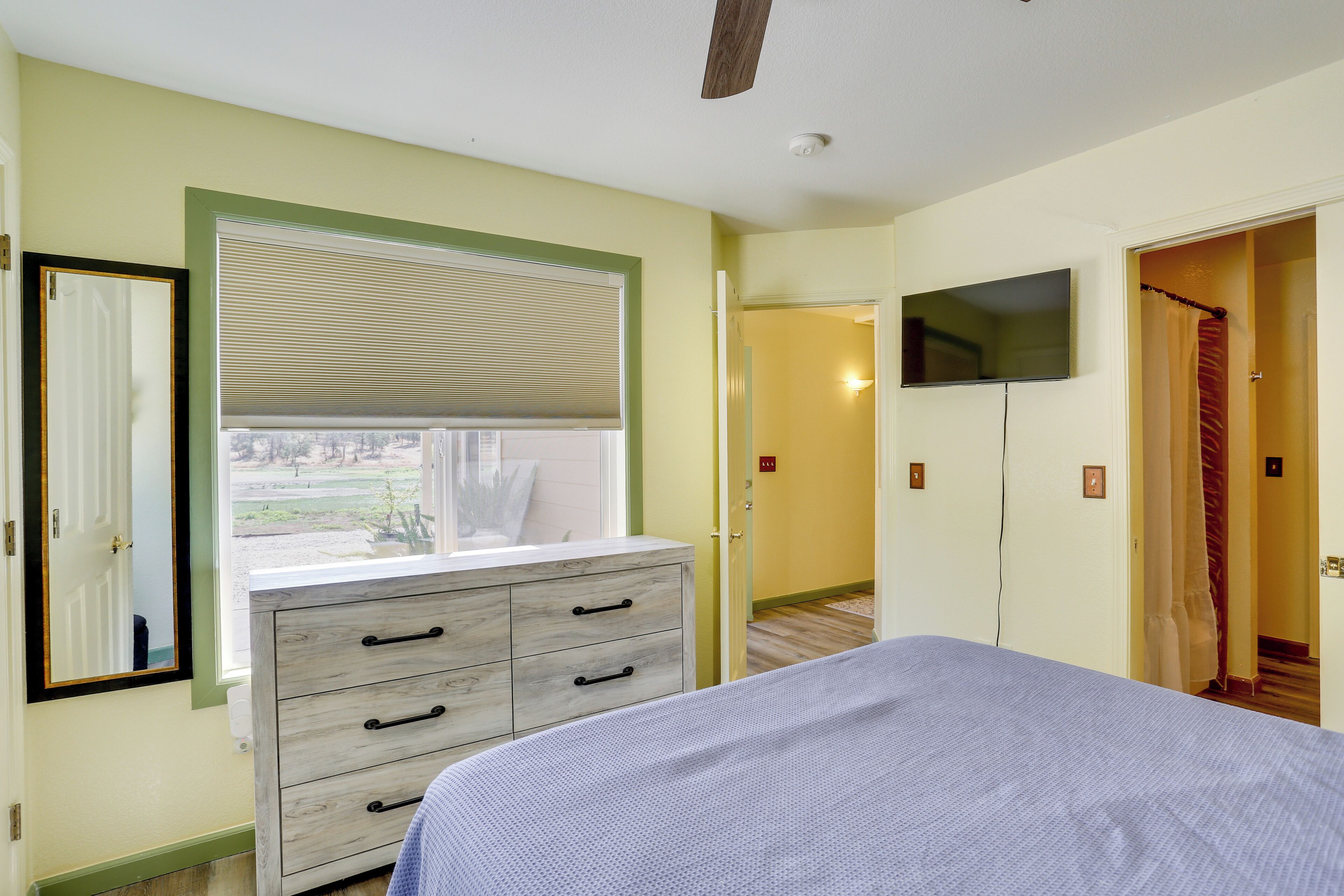 Un dormitorio con cama, cómoda, ventana con persianas y televisión en la pared.