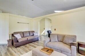 Een ruime woonkamer met een bruine leren bank, een beige fauteuil en een houten dienbladtafel.