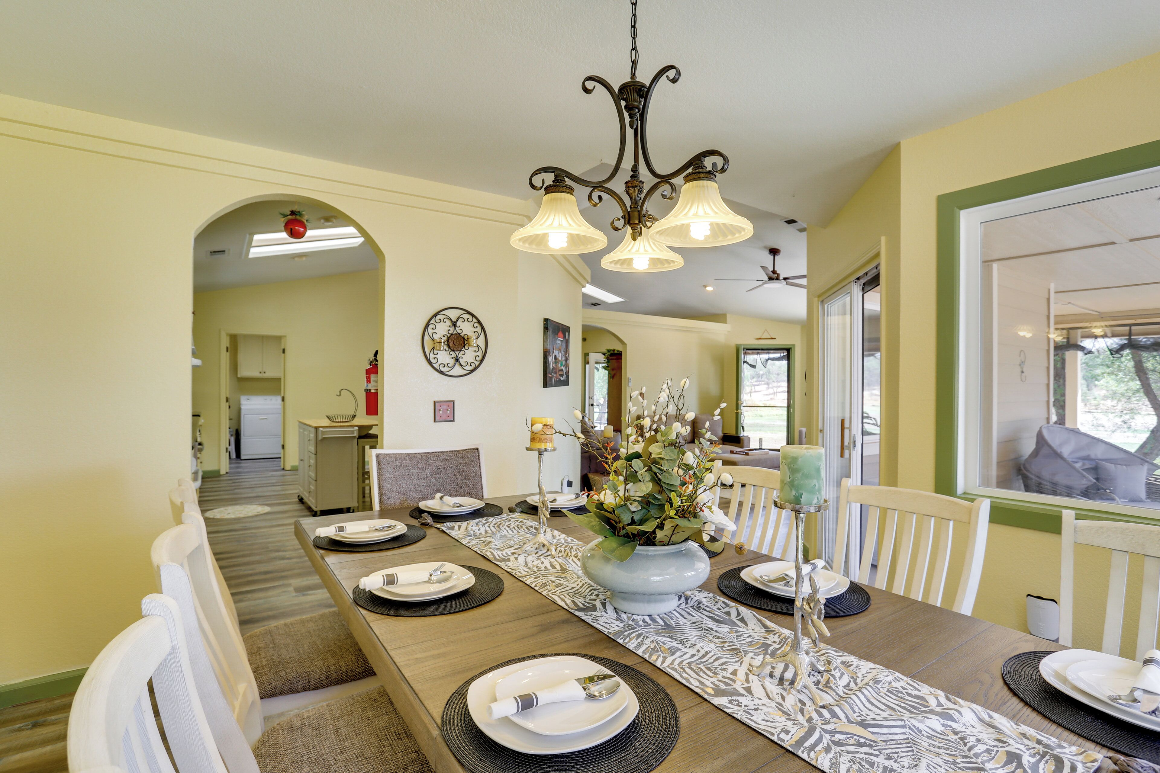 A dining area with a long table set for a meal, a chandelier, and a view of the outdoors.