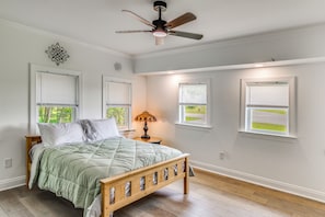 Ein Schlafzimmer mit einem Bett, einem Deckenventilator und drei Fenstern.